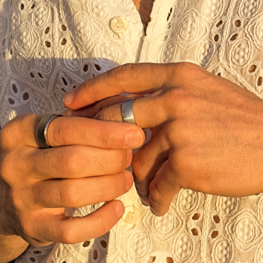 Man bär en silverfärgad tungstenring i solnedgångsljus, fokus på händer.#en:color_silver,sv:farg_silver