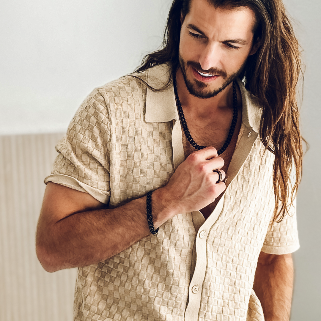 Man i mönstrad skjorta bär smyckesetet, avslappnad attityd med maskulin stil.#en:color_black,sv:farg_svart