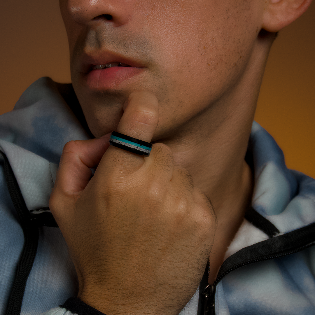 Man i blågrå skjorta håller handen mot hakan, ringen i turkos skimrar subtilt.