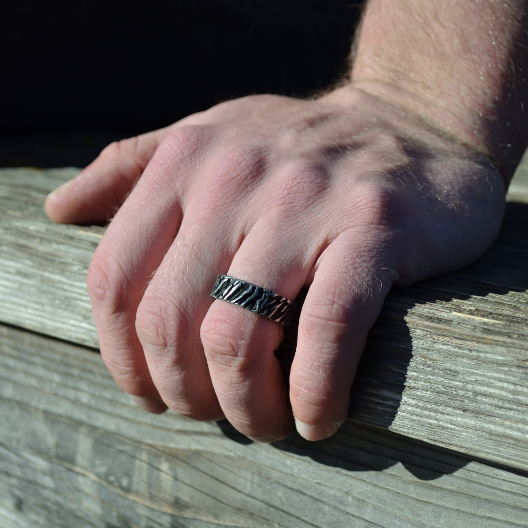 Närbild på händer vilande mot träyta, grovt mönstrad stålring ger robust känsla.