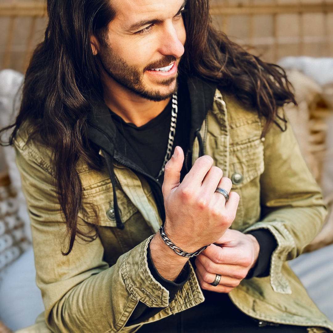 Man i grön jacka visar upp armbandet, avslappnat poserande med självsäker utstrålning.#en:color_black,sv:farg_svart