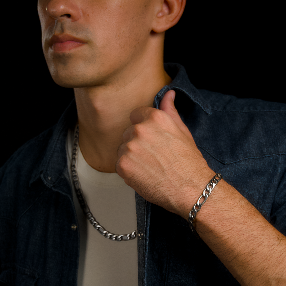 Armbandet syns tydligt när han drar av sig skjortan – silverdetaljer mot solbränd hud.#en:color_silver,sv:farg_silver