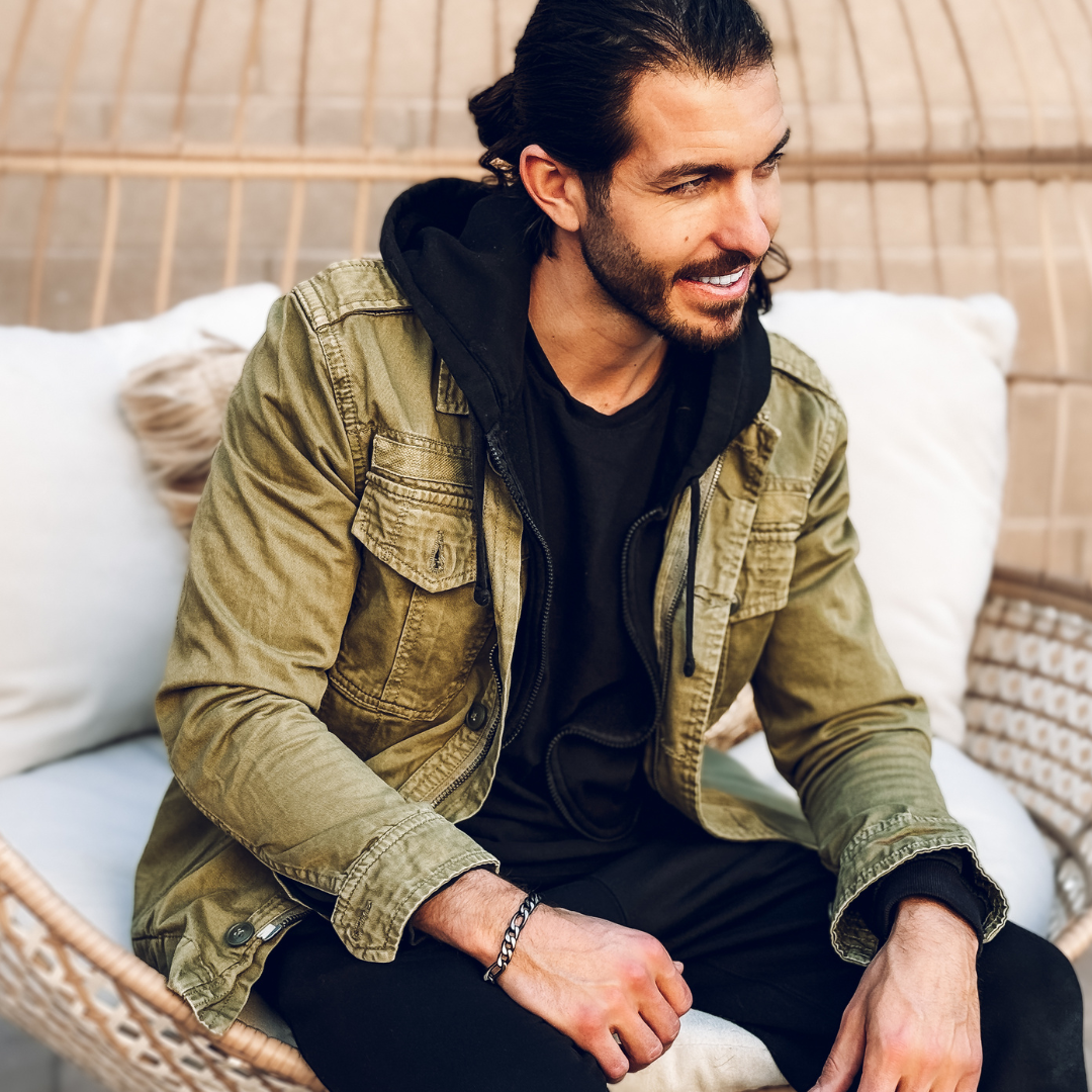 Sittande man med stilren outfit och armbandet i fokus – urban känsla i naturligt ljus.#en:color_black,sv:farg_svart