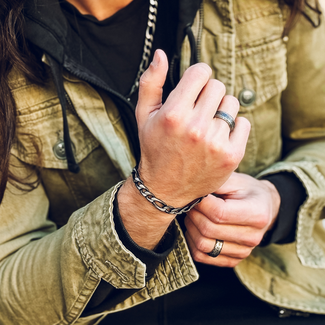 Närbild på handled vilande i knät, kedjearmbandet syns tydligt mot svart tröja.#en:color_black,sv:farg_svart