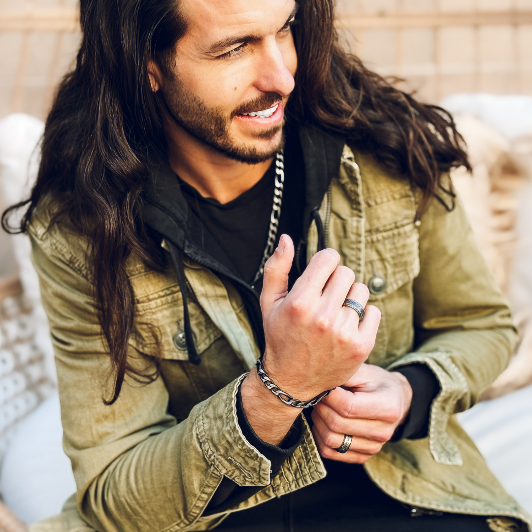 Leende man med långt hår bär armbandet, avslappnad look i vardagsmiljö.#en:color_black,sv:farg_svart