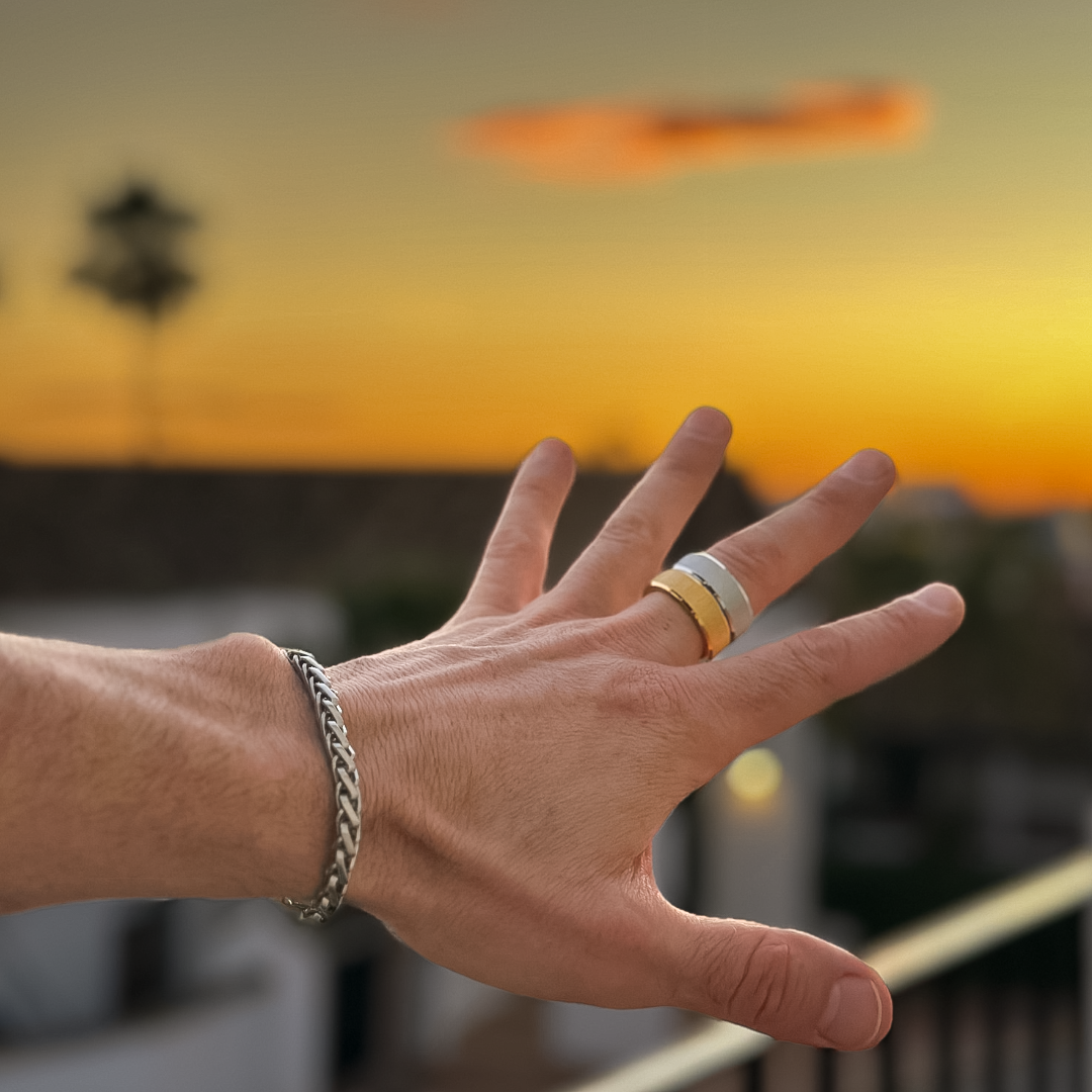 Man bär silverring i solnedgång, handen lyfts mot en varm kvällshimmel.#en:color_silver,sv:farg_silver