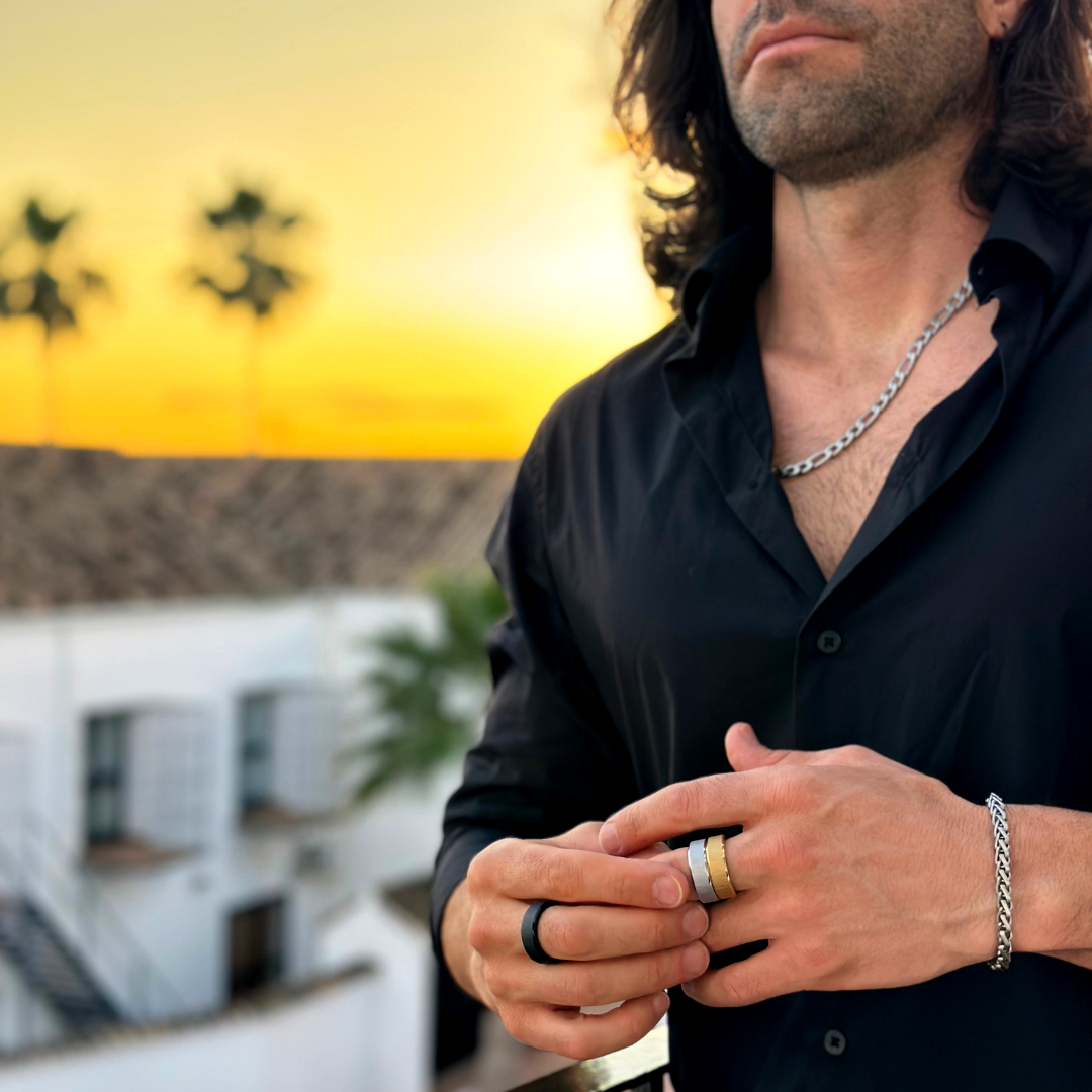 Man i svart skjorta på takterrass i kvällsljus, visar olika färgar ringar och armband.#en:color_black,sv:farg_svart