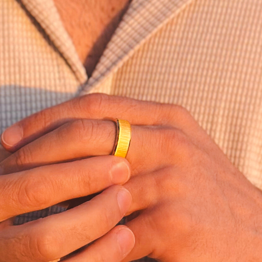 Närbild på man som bär guldring i rostfritt stål, beige skjorta i bakgrunden.#en:color_gold,sv:farg_guld