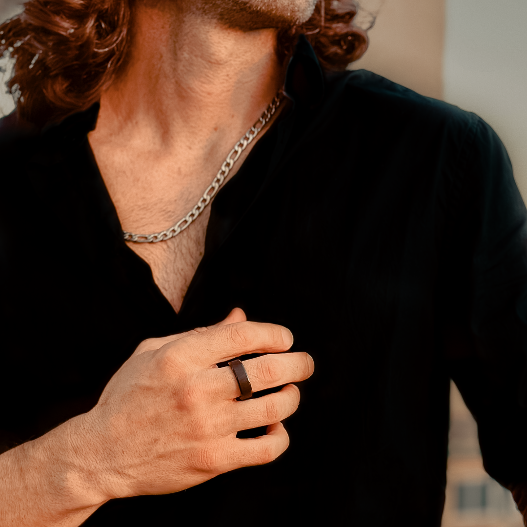 Man med lockigt hår och svart skjorta bär stilren svart ring.#en:color_black,sv:farg_svart