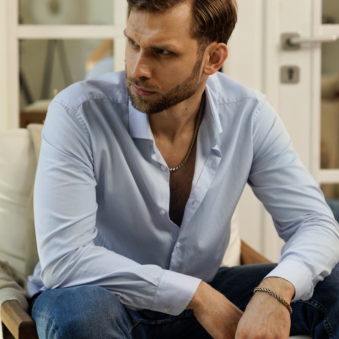 Man wearing a light blue shirt and jeans sitting on a couch.
#en:color_gold,sv:farg_guld