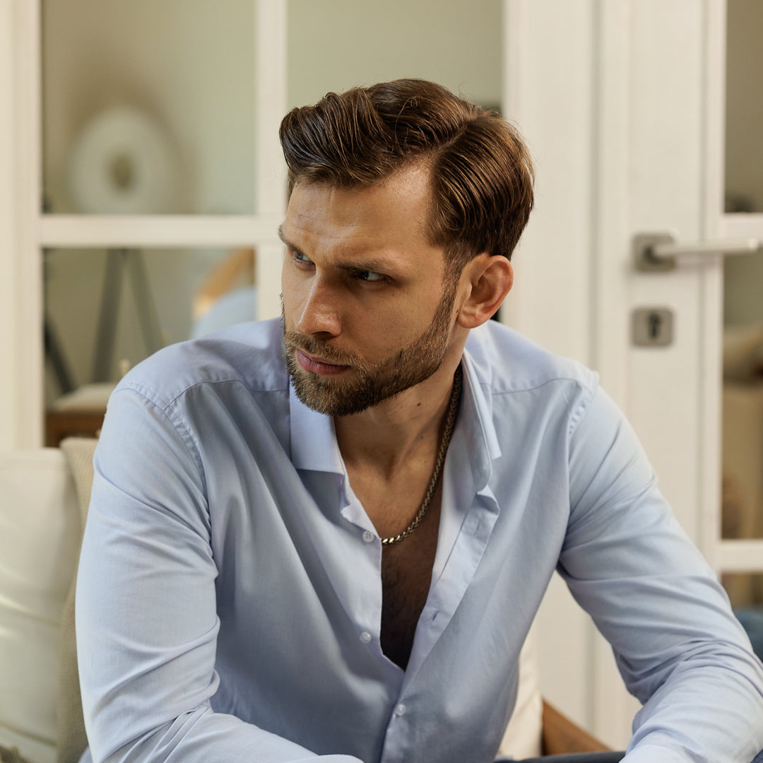 Man with a beard wearing an open light blue shirt in a blurred indoor setting.
#en:color_gold,sv:farg_guld