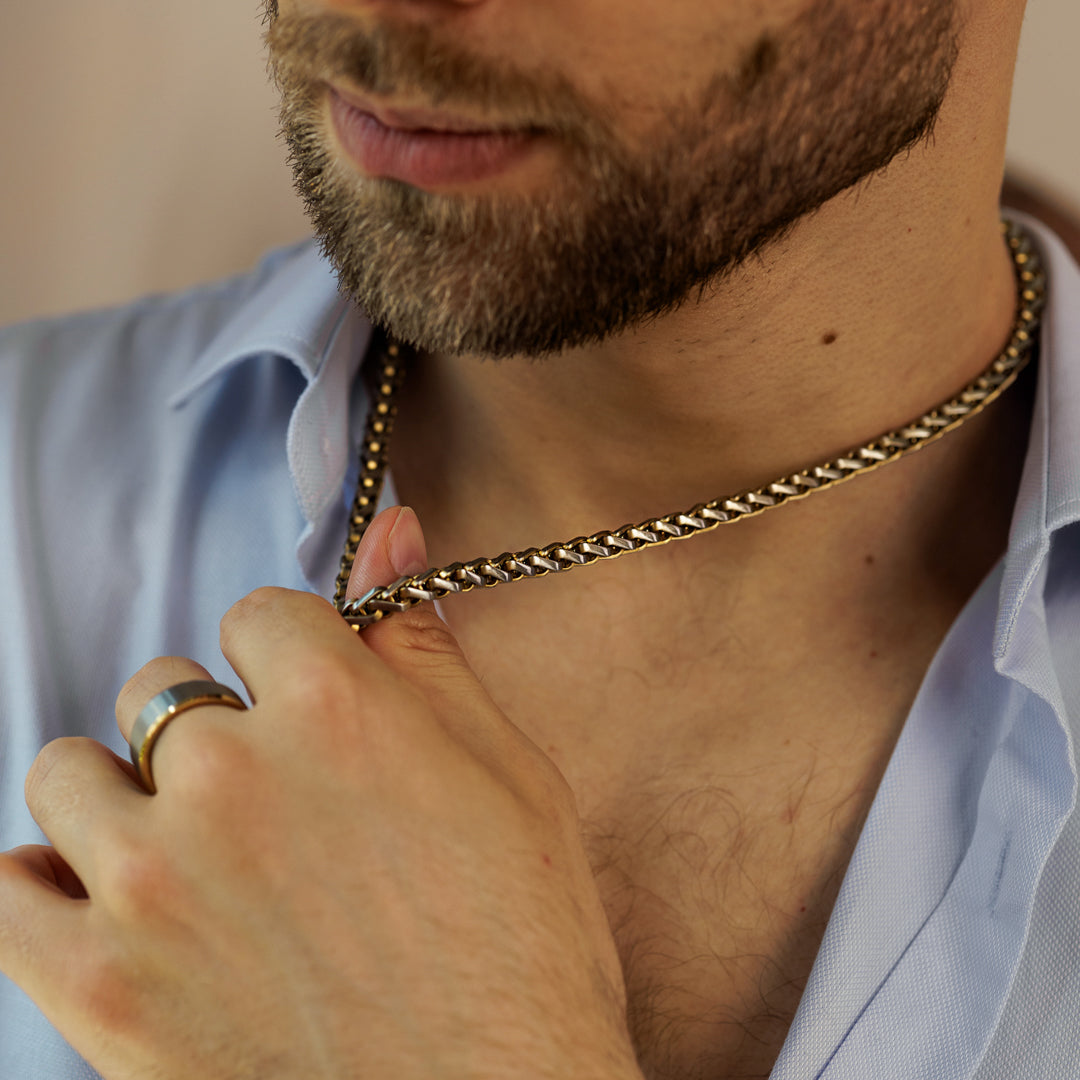 Man adjusting a gold chain necklace with a blurred background.
#en:color_gold,sv:farg_guld