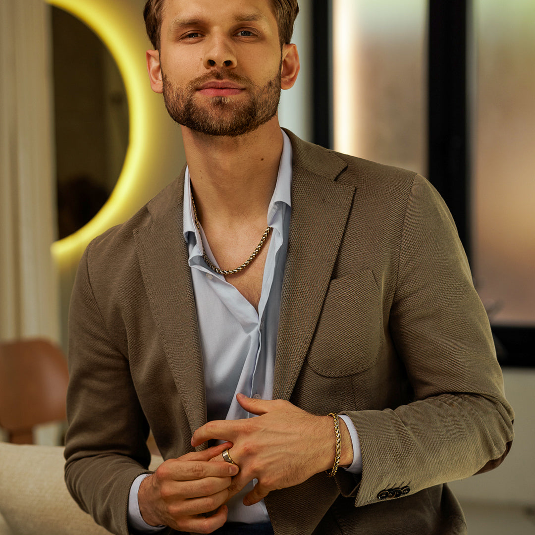 Man wearing a brown blazer over a light blue shirt with a blurred indoor background.
#en:color_gold,sv:farg_guld