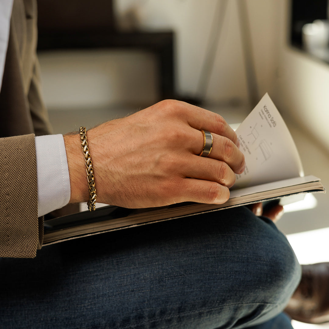 Person holding a book with a gold ring and bracelet, sitting on a couch.
#en:color_gold,sv:farg_guld