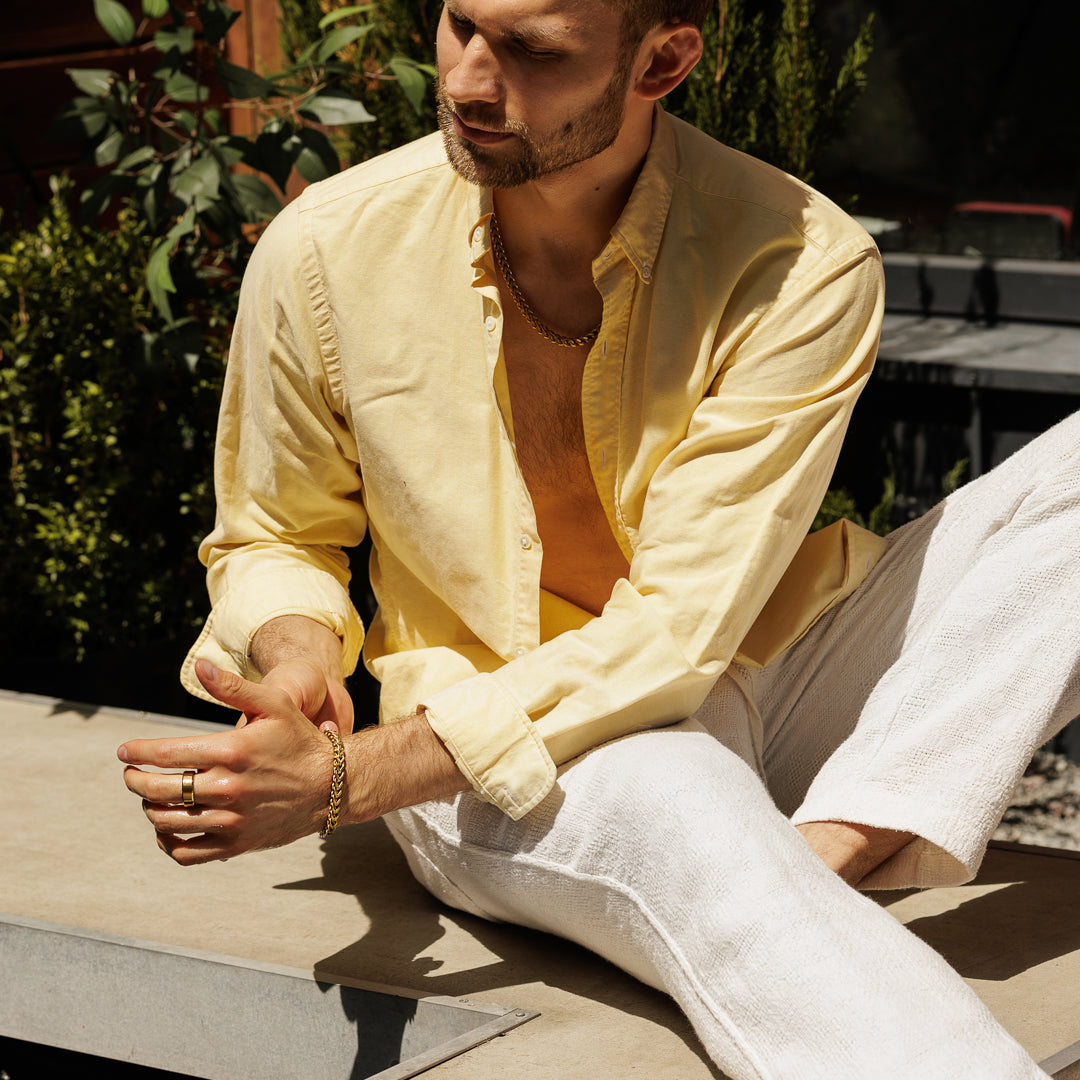 Man wearing a light yellow shirt and white pants sitting outdoors.
#en:color_gold,sv:farg_guld