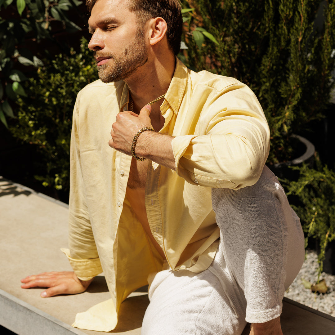 Man in a yellow shirt and white pants sitting outdoors with greenery in the background.
#en:color_gold,sv:farg_guld