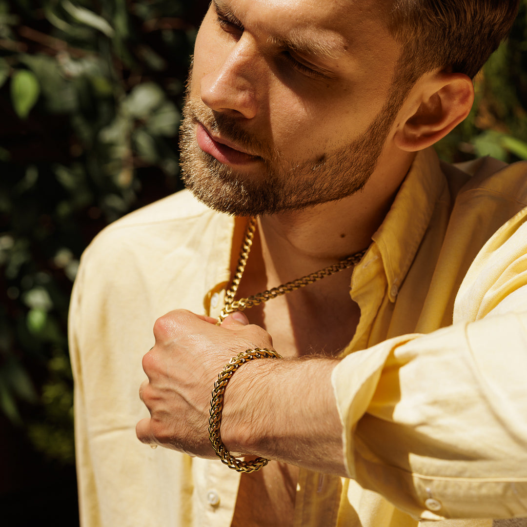 Man wearing a gold chain and bracelet with a blurred green background.
#en:color_gold,sv:farg_guld