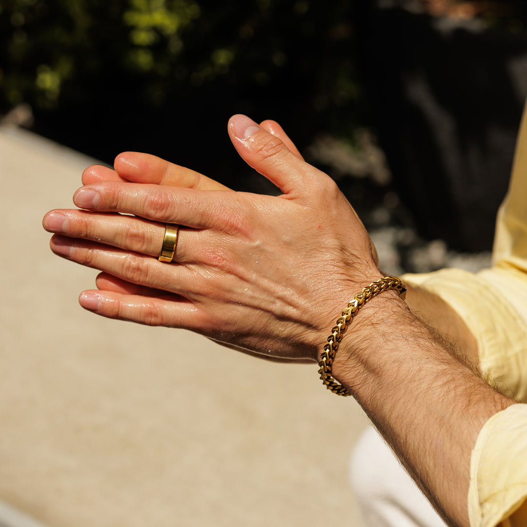 Hand with gold ring and bracelet against a blurred outdoor background.
#en:color_gold,sv:farg_guld