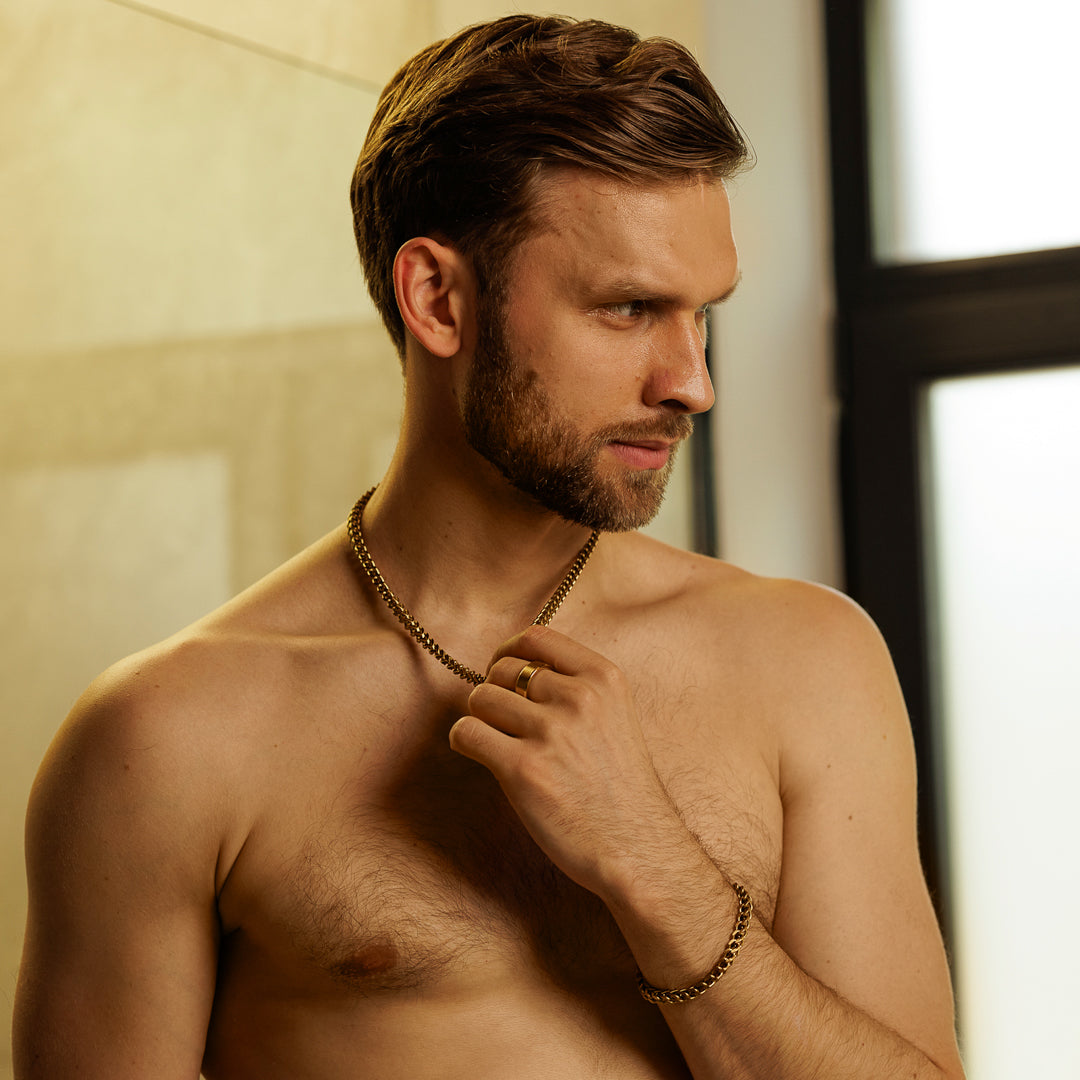 Man with a necklace adjusting it in a bathroom setting.
#en:color_gold,sv:farg_guld