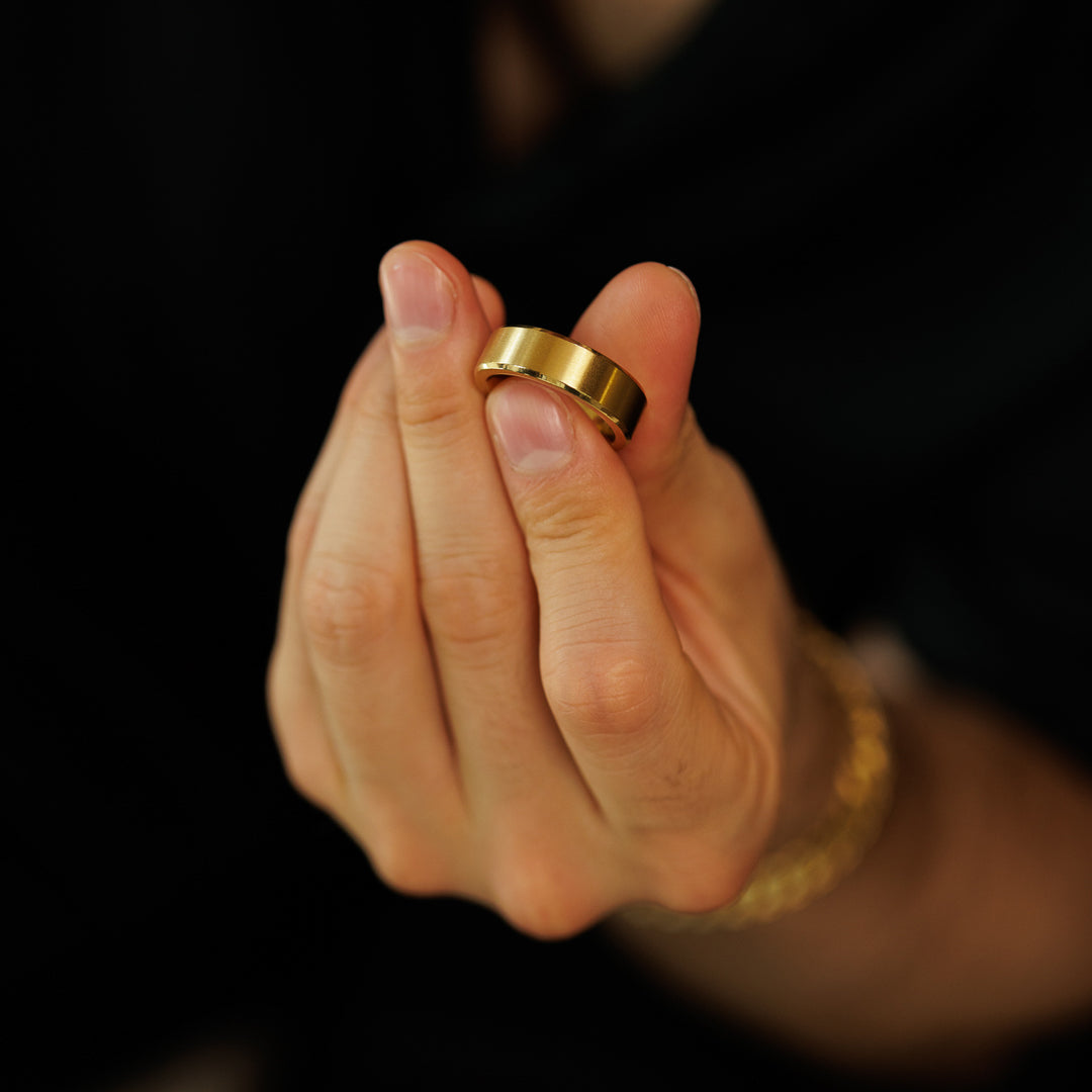 Hand holding a gold ring against a dark background.
#en:color_gold,sv:farg_guld