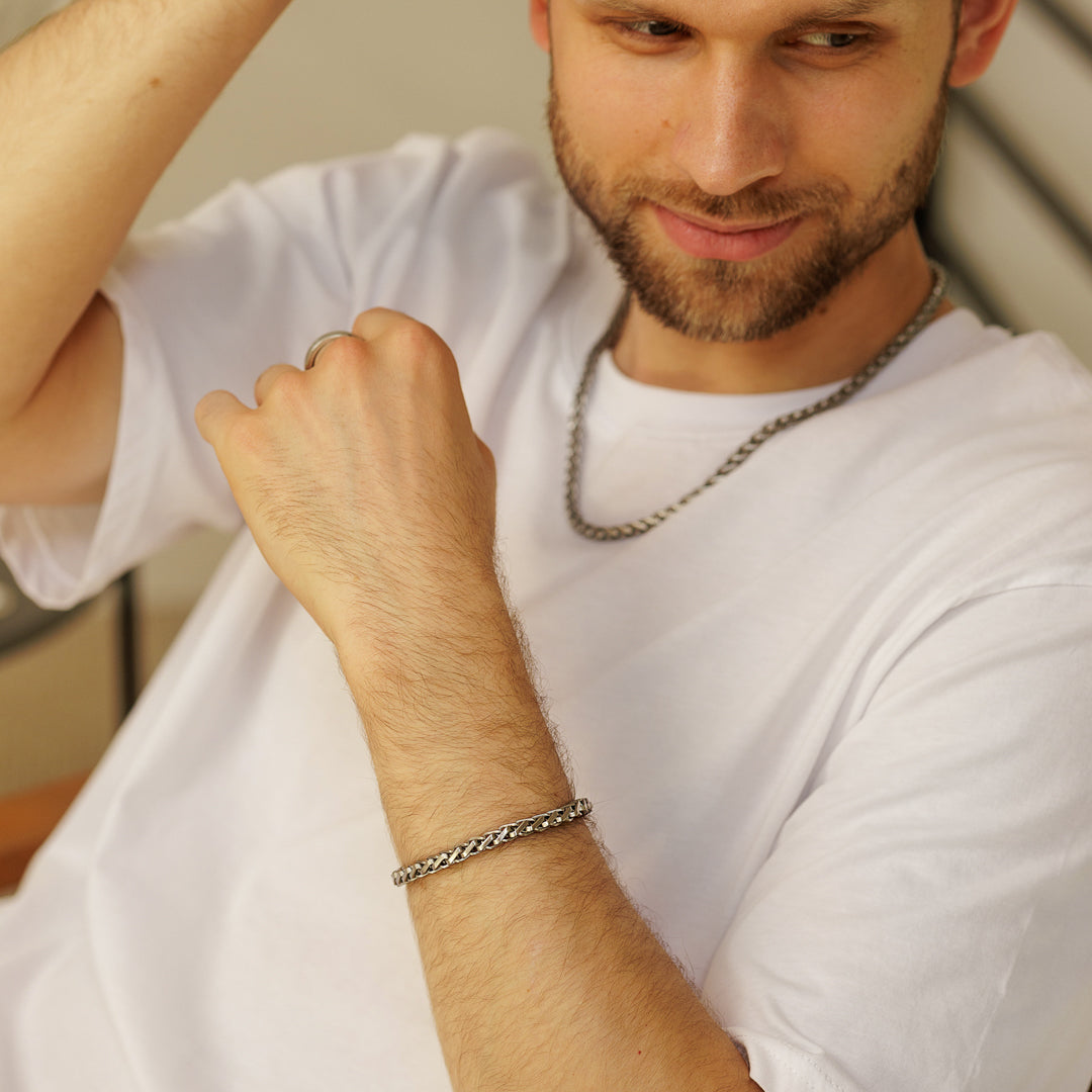 Man wearing a silver chain necklace and bracelet, sitting indoors.
#en:color_silver,sv:farg_silver