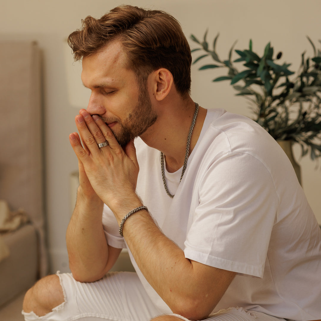 Man in a white t-shirt sitting on a bed with his head in his hands, looking distressed.
#en:color_silver,sv:farg_silver