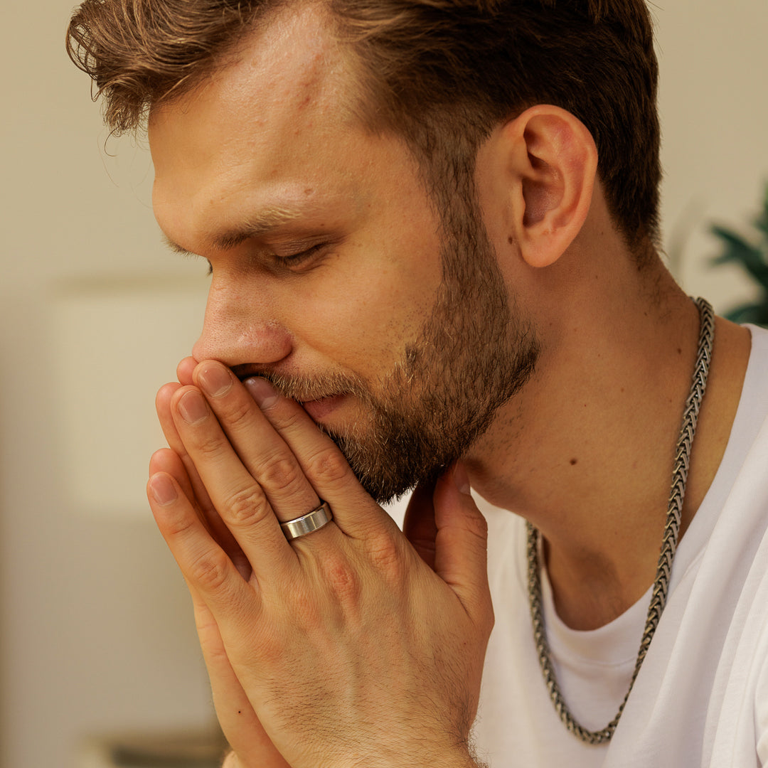 Man with a beard and chain necklace looking down with hand on chin.
#en:color_silver,sv:farg_silver