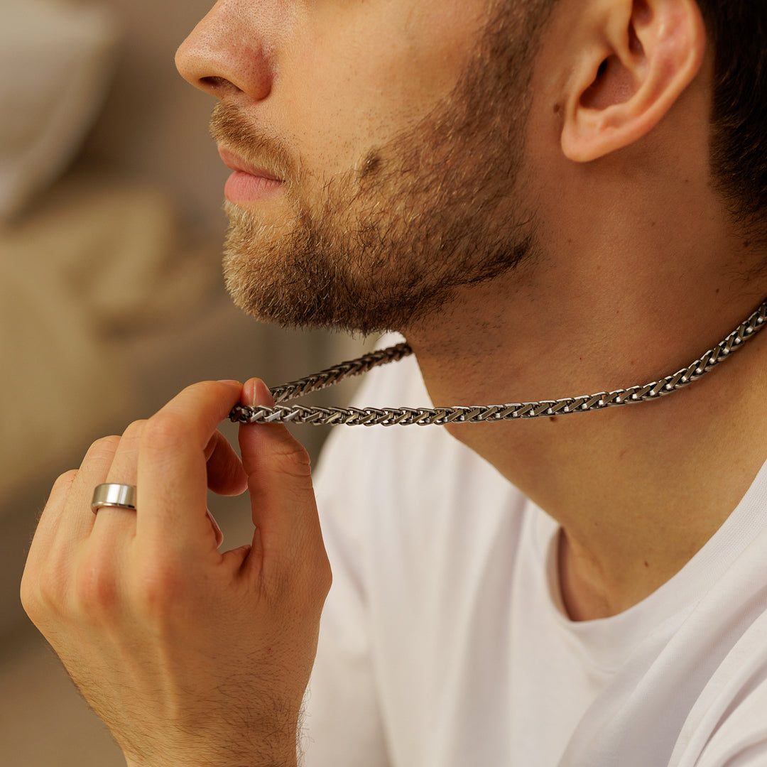Man adjusting a chain necklace with a neutral background.
#en:color_silver,sv:farg_silver