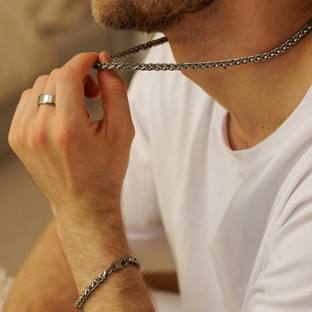 Person holding a silver chain necklace with a neutral background.
#en:color_silver,sv:farg_silver