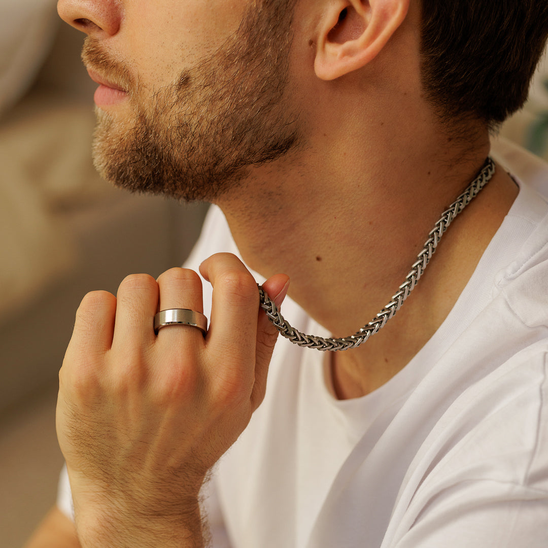 Man adjusting a silver chain necklace with a blurred background.
#en:color_silver,sv:farg_silver