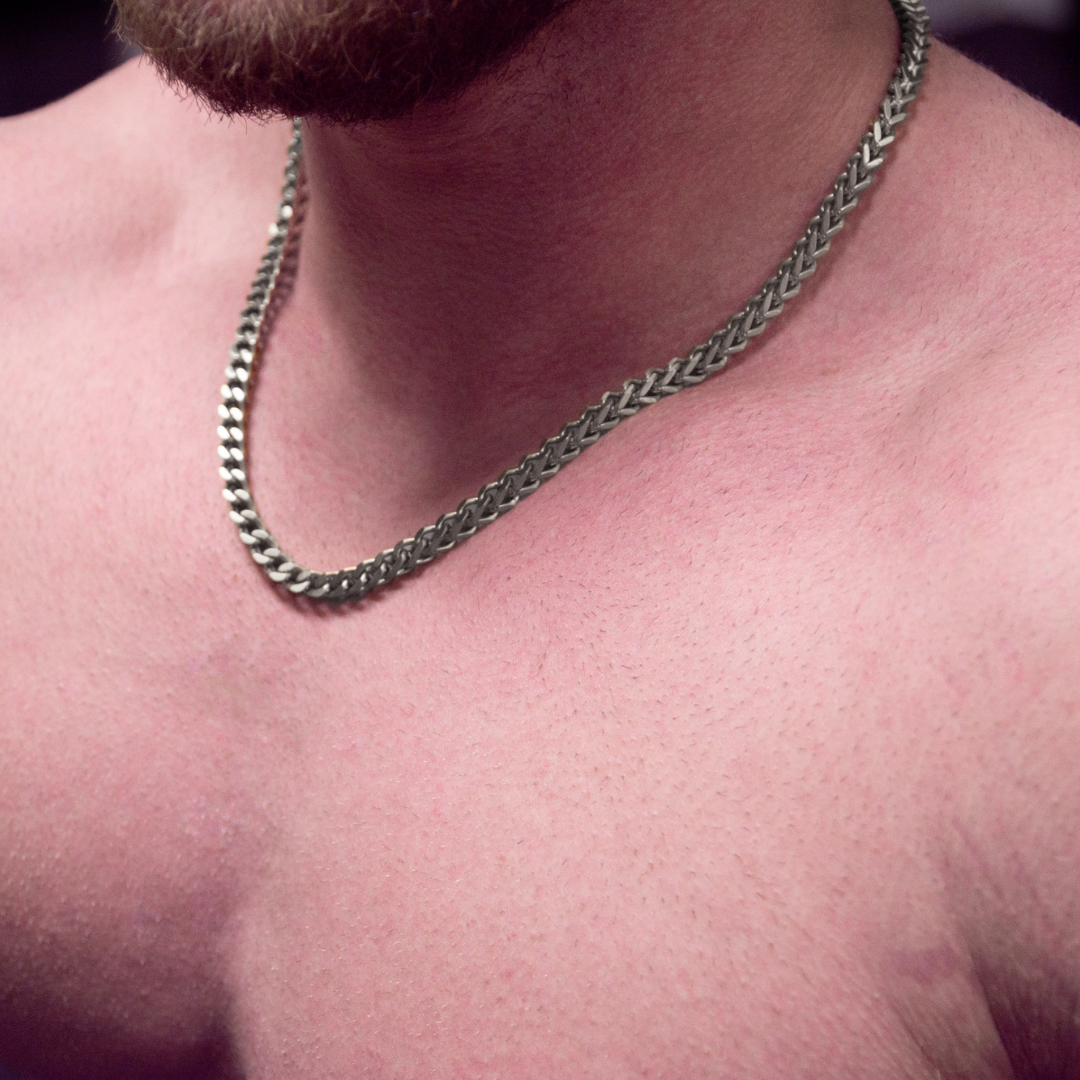 Närbild på hals med silverkedja, muskulös överkropp och varm belysning.#en:color_silver,sv:farg_silver