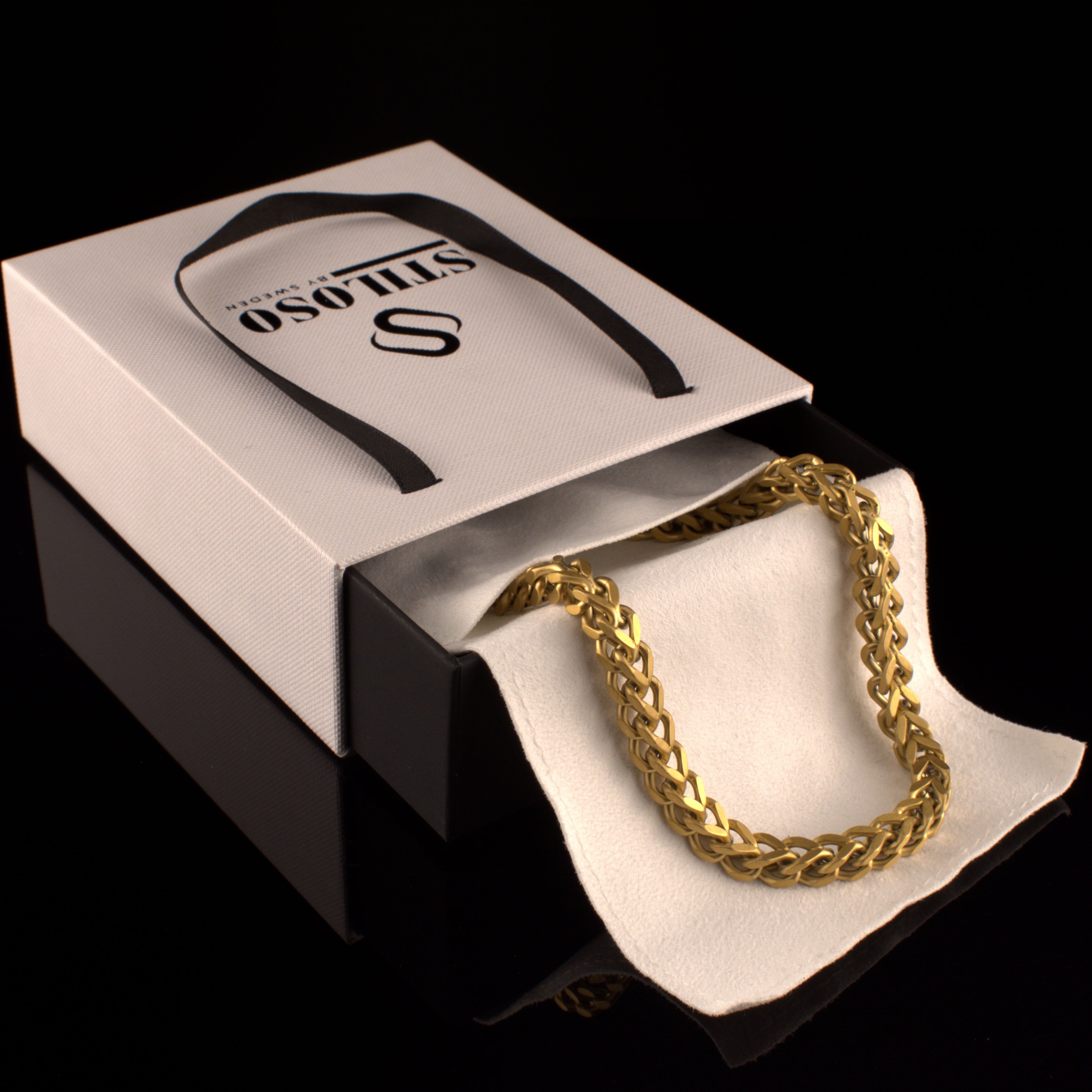 Guldfärgat armband i lyxig ask med Stiloso-logga, elegant uppvisat från sidan.#en:color_gold,sv:farg_guld