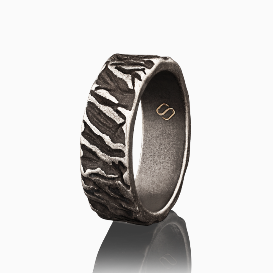 Texturerad ring i rostfritt stål med rå yta och Stiloso-logga, frilagd mot vit bakgrund.