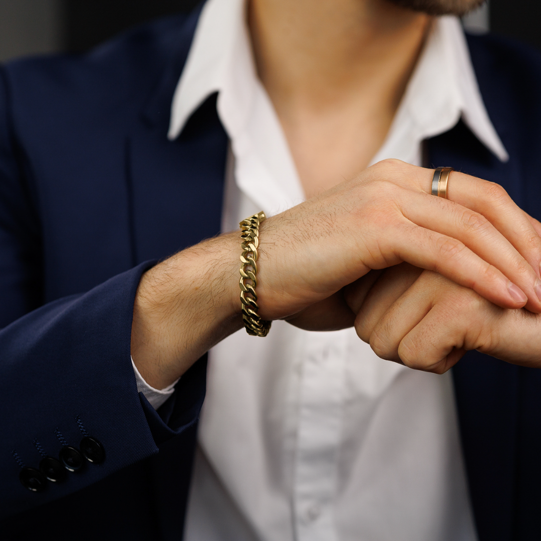 Man i blå kavaj med guldarmband, ser avslappnad men stilren ut.#en:color_gold,sv:farg_guld