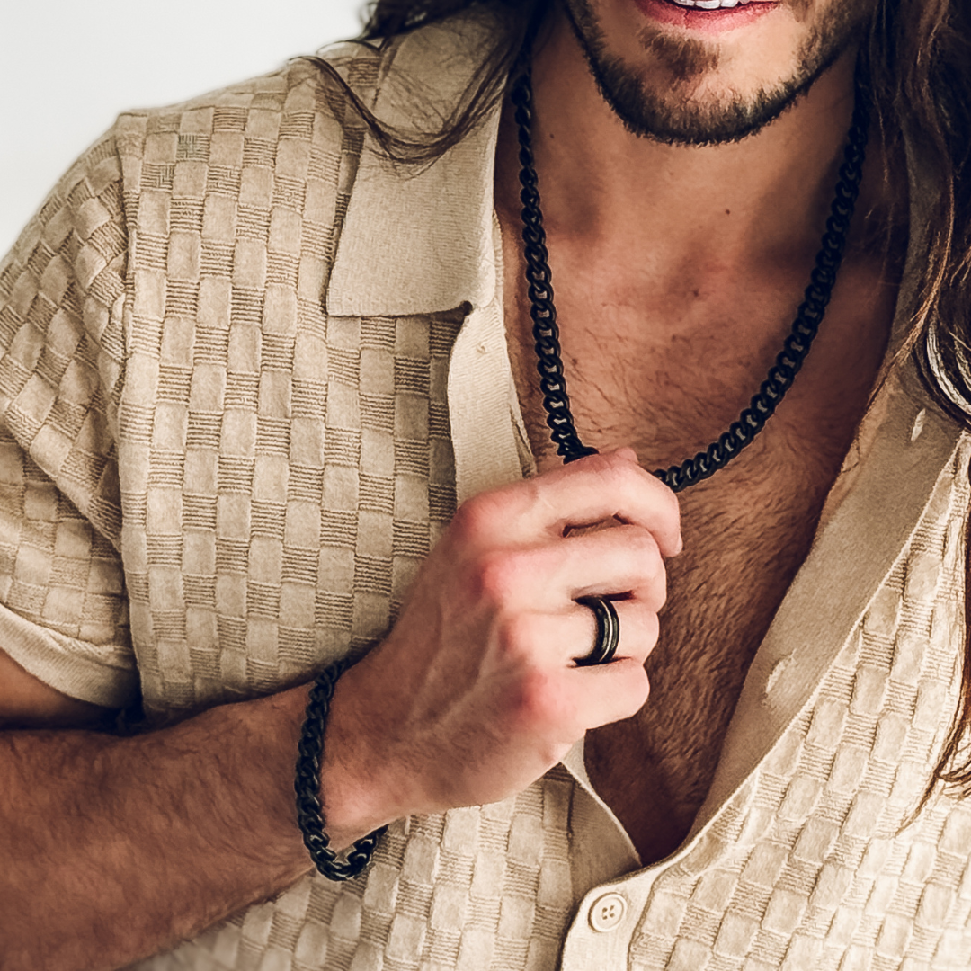 Långhårig man i beige skjorta bär silverarmband.#en:color_black,sv:farg_svart