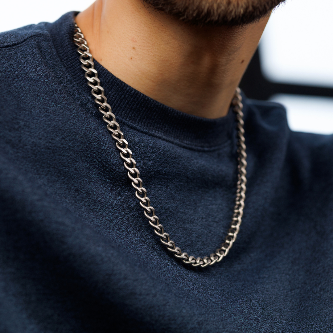 Man i marinblå tröja med svart kedja, stilrent och avslappnat uttryck.#en:color_silver,sv:farg_silver