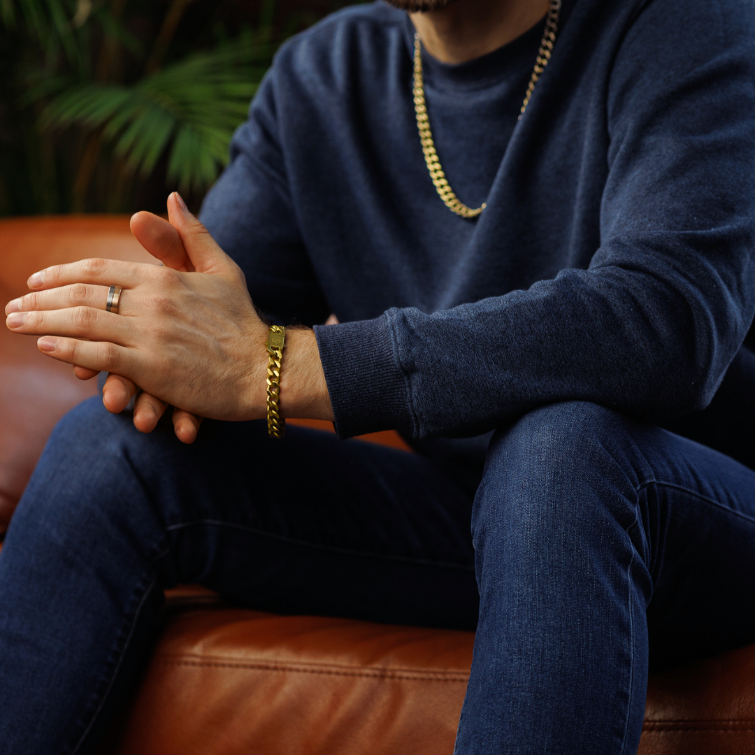 Man i mörk tröja med armbandet och kedjan, avslappnad pose med exklusiv känsla.#en:color_gold,sv:farg_guld