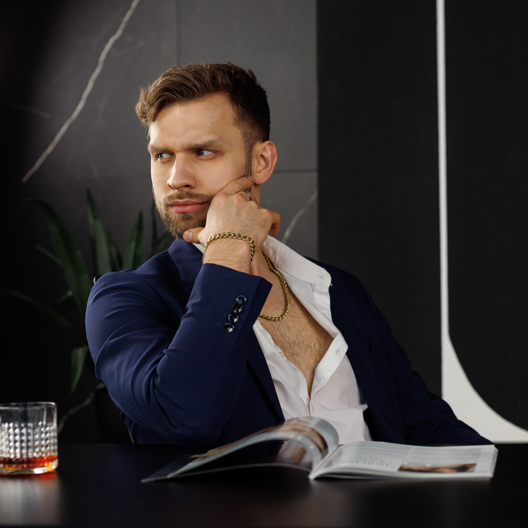 Halskedjan syns under kavajen, armbandet kompletterar looken – modern lyx i fokus.#en:color_gold,sv:farg_guld