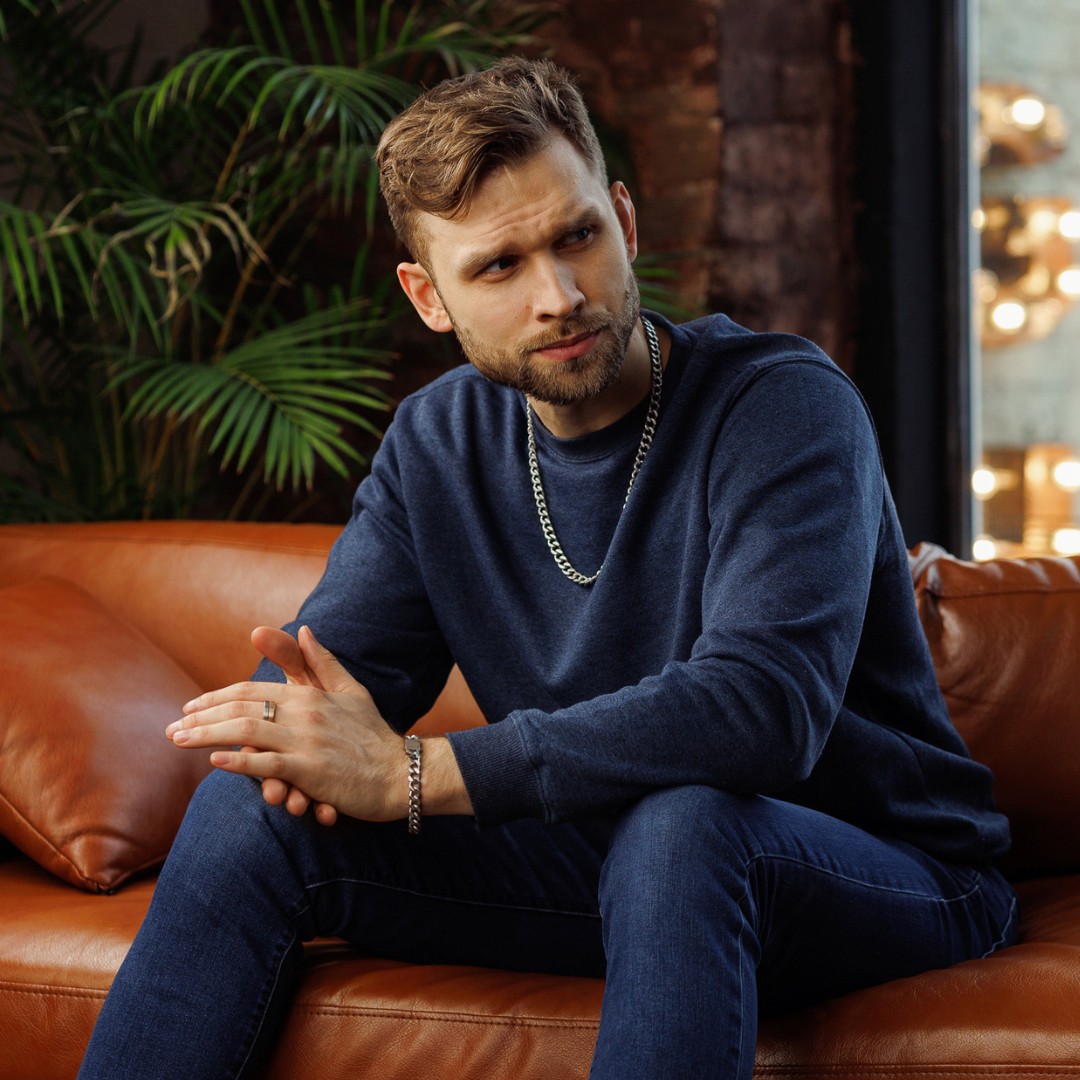 Sittande man i soffa, smyckesetet ger en sofistikerad helhet.#en:color_silver,sv:farg_silver