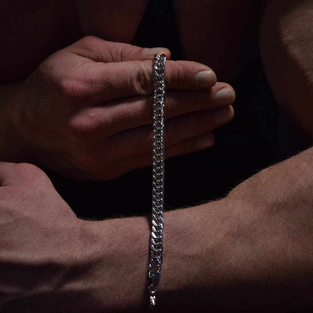 Armbandet hänger i handen, biceps i fokus – stark visuell kontrast.#en:color_silver,sv:farg_silver