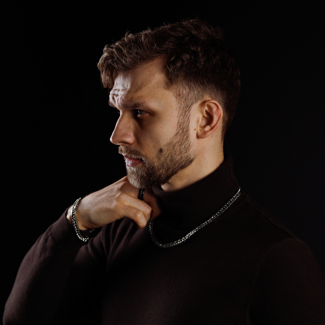 Man i svart polotröja justerar silverkedjan, elegant och stilren look.#en:color_silver,sv:farg_silver