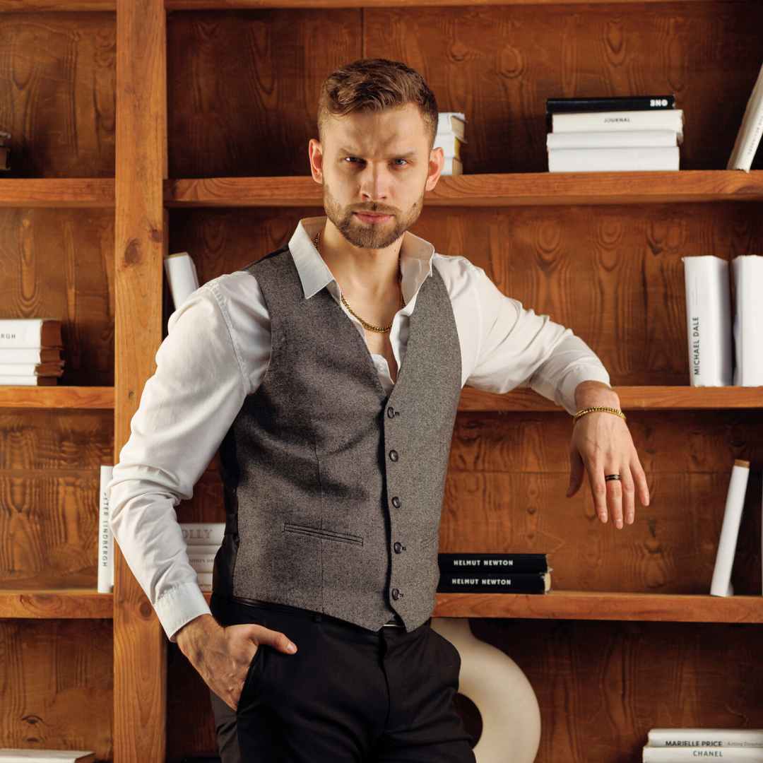Man i grå väst bär smyckesetet – tidlös look med modern twist.#en:color_gold,sv:farg_guld