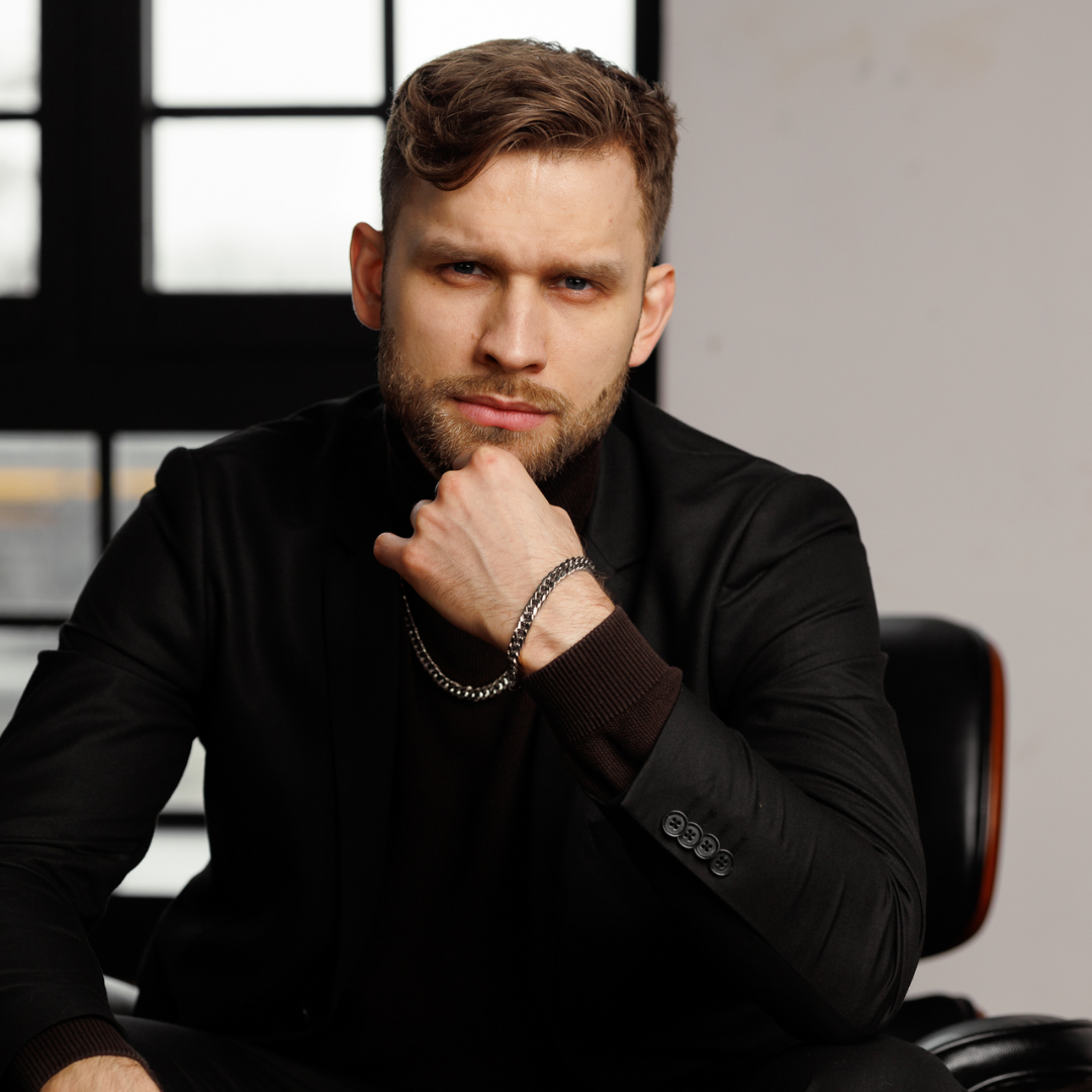 Man i svart kavaj bär setet, poserar självsäkert vid skrivbord i dagsljus.
#en:color_silver,sv:farg_silver