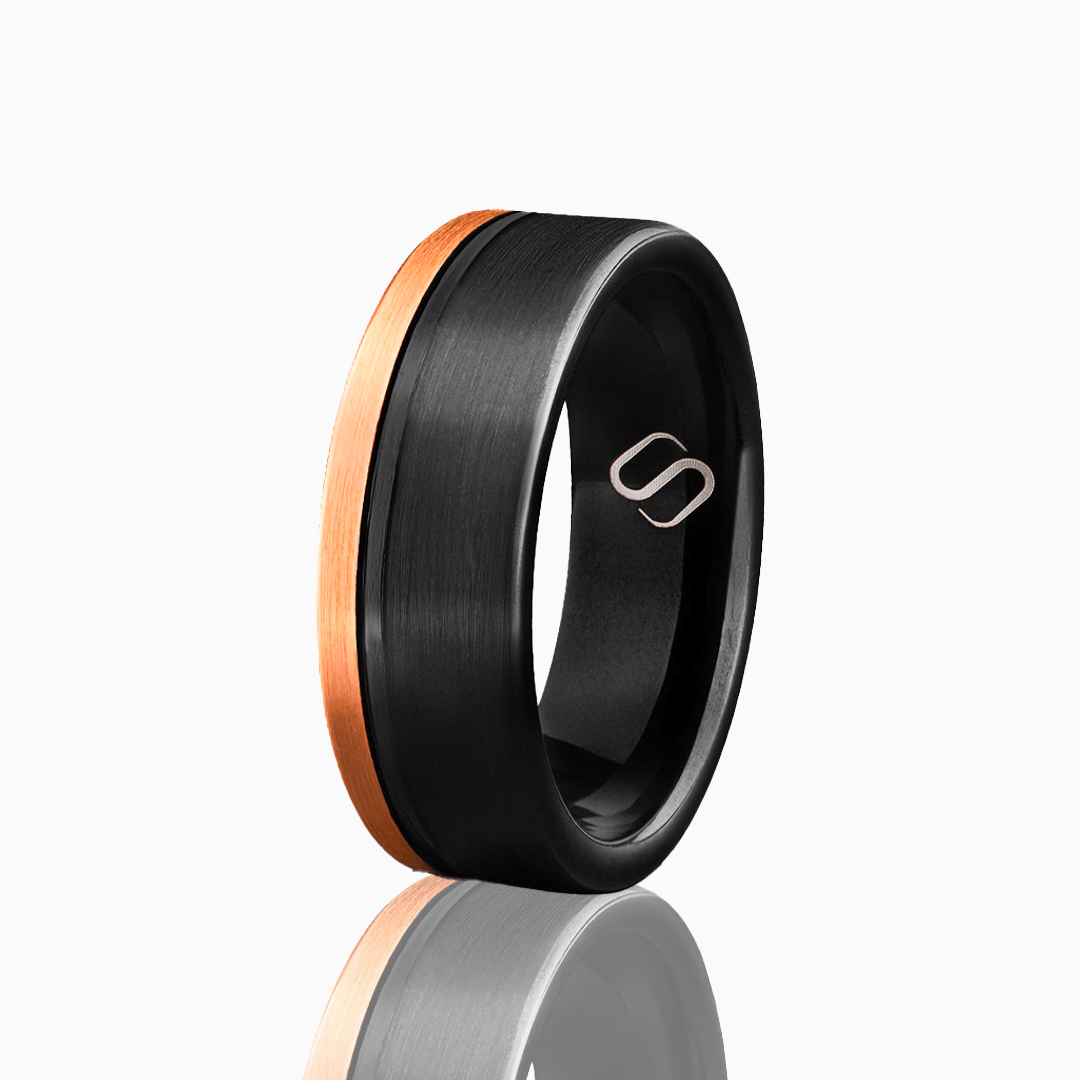 Svart tungstenring med kopparfärgad kant och Stiloso-gravyr, frilagd mot vit bakgrund.