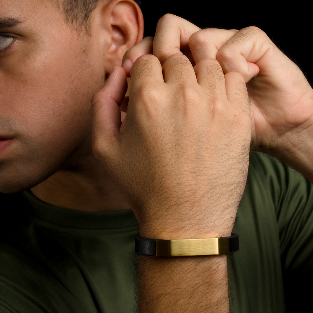 Man i grön t-shirt justerar armbandet, guldig yta fångar ljuset fint.
#en:color_gold,sv:farg_guld