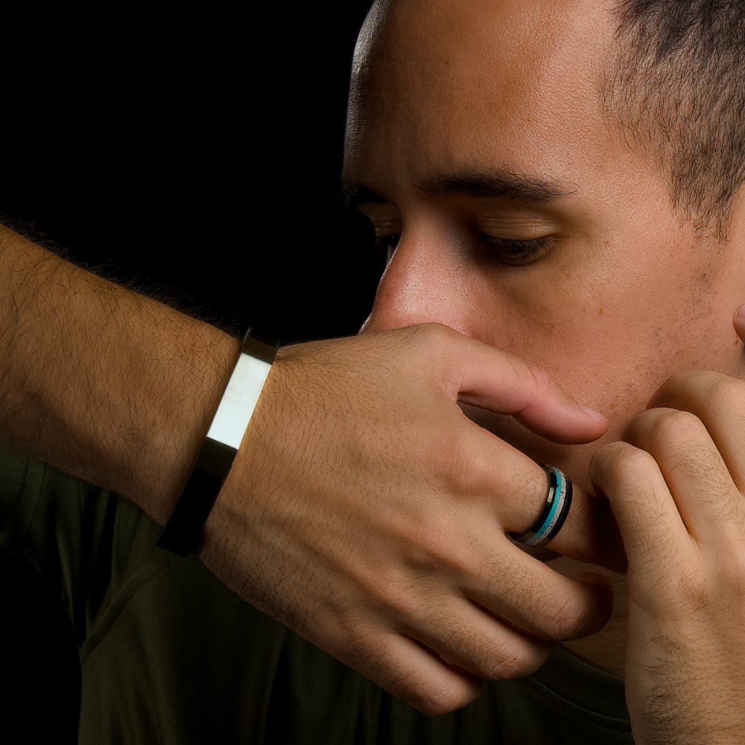 Man vilar ansiktet mot handen, armbandet blänker diskret i mjukt ljus.#en:color_silver,sv:farg_silver