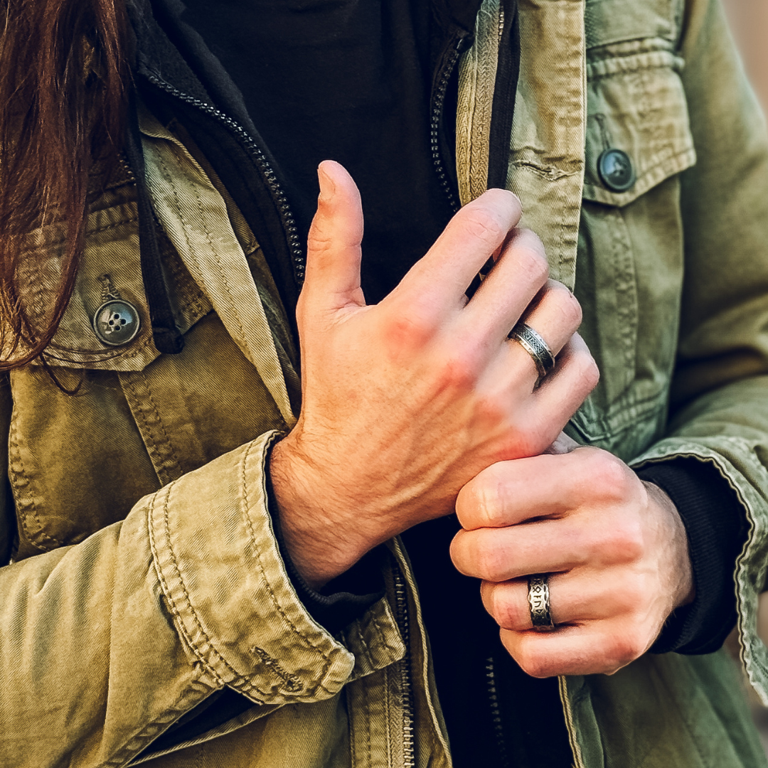 Hand över bröstet, fokus på den kraftfulla stålringen med vikingainspirerad runskrift.