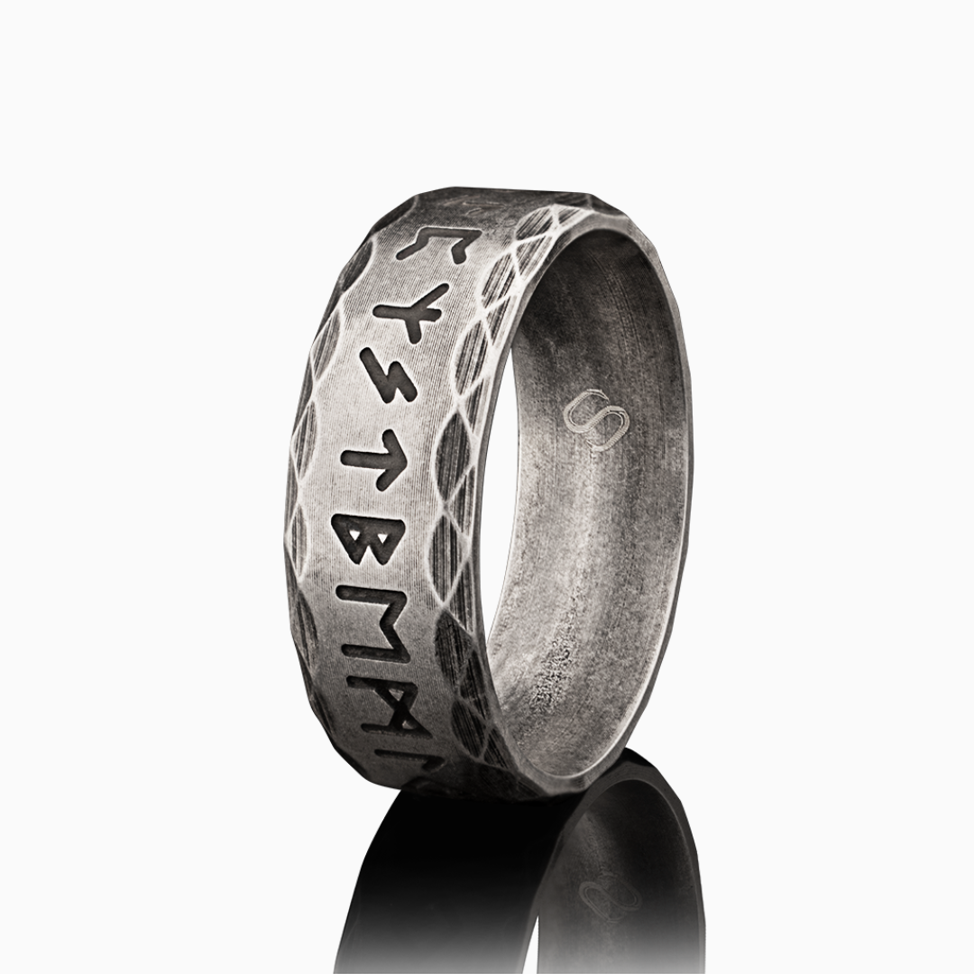 Bred ring i antikbehandlat rostfritt stål med djupgraverade runor, frilagd mot vit bakgrund.