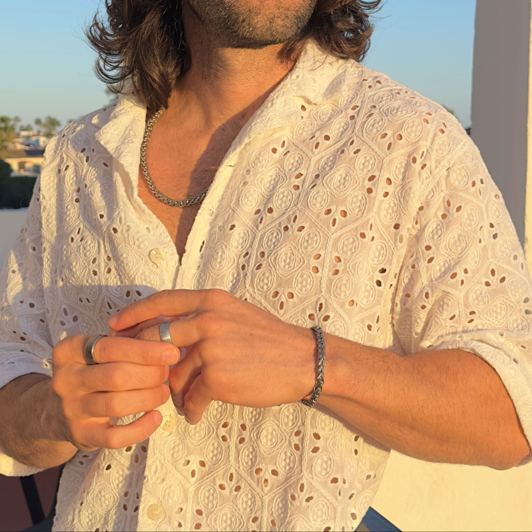 Man i vit skjorta visar upp en silverring och ett armband i naturligt kvällsljus.#en:color_silver,sv:farg_silver