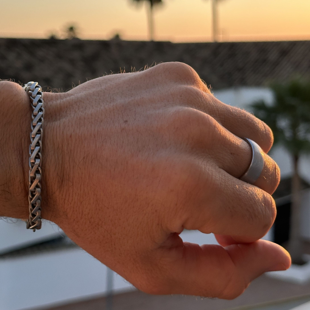 Närbild på hand som bär både silverring och armband vid solnedgång.#en:color_silver,sv:farg_silver